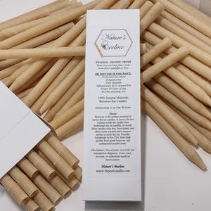 Puede incluir: Velas para oídos de cera de abejas de Nature's Beeline. La imagen muestra una caja de velas y una pila de velas enrolladas de color beige. El embalaje del producto incluye texto sobre las características e instrucciones de uso.