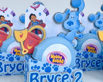 May include: Blue's Clues-themed party favors. Each box features a blue paw print design, the name "Bryce" in silver glitter, and a number "2". The boxes contain a light blue bubble gum container with the text "Hubba Bubba".