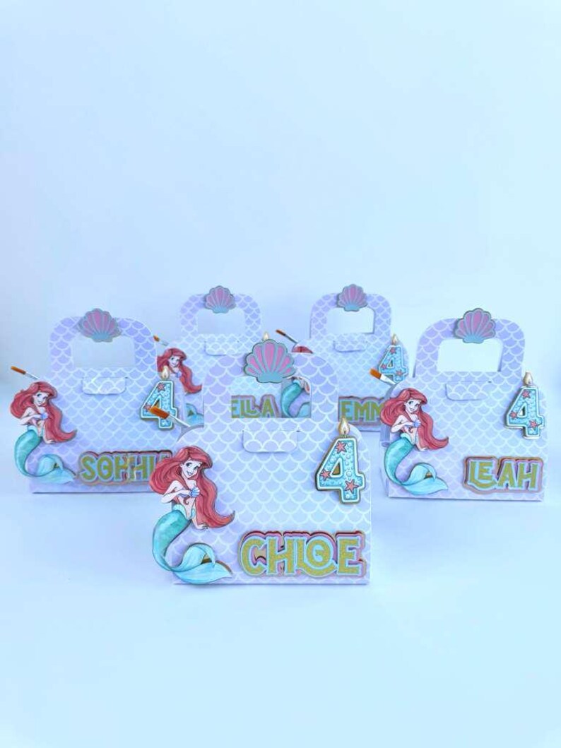 May include: A set of five light purple gift boxes with a mermaid scale pattern. Each box features a cutout handle, a pink seashell accent, a cartoon mermaid illustration, a number four, and a personalized name in green and gold lettering.