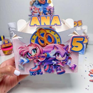 May include: A custom-made birthday party favor box featuring Sonic the Hedgehog characters. The box is decorated with the name "ANA" and the number "5". The design includes images of Amy Rose and Blaze the Cat on roller skates.