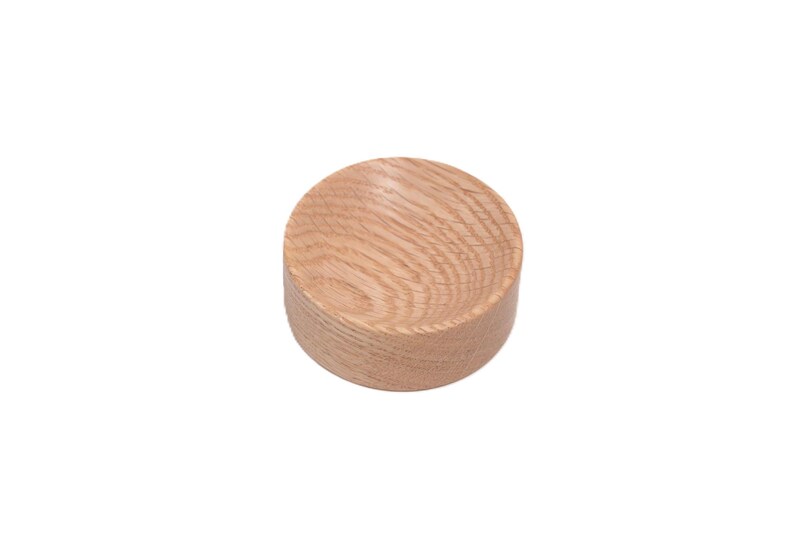 May include: A small, round wooden bowl with a natural wood finish. The bowl is made of oak and has a smooth, polished surface.