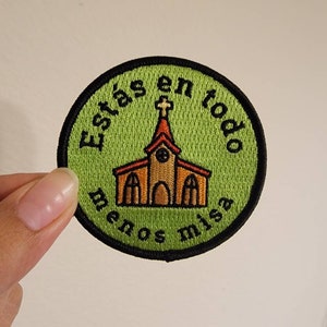 May include: A green and black embroidered patch with a church building in the center. The text around the church reads "Estás en todo menos misa".