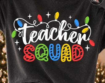 May include: A charcoal gray crewneck sweatshirt featuring the white text "teacher" in a cursive script and the word "SQUAD" in bold, colorful, striped block letters. The design includes a string of multi-colored Christmas light bulbs and stars.