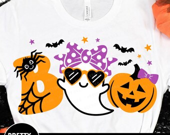 May include: A white t-shirt with a graphic design of a ghost wearing sunglasses and a bow, a spider, and a pumpkin. The text "BOO" is written in orange with a spider web design.
