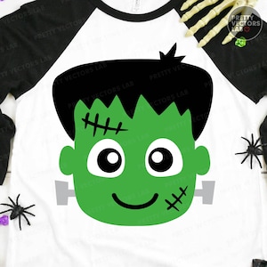 May include: White raglan-sleeve shirt with a green Frankenstein's monster face graphic. The graphic features a green face with black hair, stitches, and a smiling mouth. The sleeves are black. The shirt is perfect for Halloween.