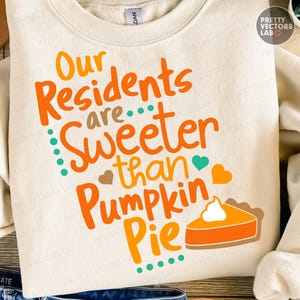 May include: Cream-colored sweatshirt with the text "Our Residents are Sweeter than Pumpkin Pie" in orange and teal lettering. A graphic of a pumpkin pie slice is also included. The sweatshirt is a crew neck style.