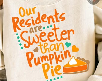 Puede incluir: Sudadera color crema con el texto "Our Residents are Sweeter than Pumpkin Pie" en letras naranjas y turquesas. También incluye un gráfico de una porción de tarta de calabaza. La sudadera es de cuello redondo.