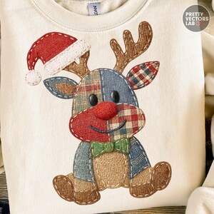 May include: Cream-colored sweatshirt featuring a patchwork reindeer design. The reindeer has a red nose, a Santa hat, and a green bow tie. The design incorporates plaid and textured fabrics, creating a festive and cozy aesthetic.