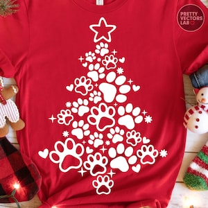 May include: A red t-shirt featuring a white graphic of a Christmas tree constructed from various sizes of animal paw prints, small hearts, and stars, topped with a large star. The text Pretty Vectors Lab is printed in the upper right corner.