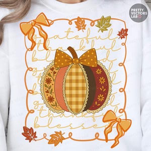 Könnte beinhalten: Weißes Sweatshirt mit einem herbstlichen Kürbisdesign. Der Kürbis hat einen braunen Stiel und ist mit orangefarbenen, braunen und gelben Mustern verziert. Die Worte "grateful, thankful, blessed" sind um den Kürbis geschrieben.