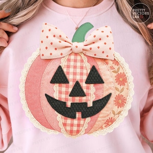 Op de afbeelding: Decoratieve pompoen-applicatie met een lachend gezicht, strik en steel. De pompoen heeft een patchwork-ontwerp met roze, rode en crèmekleuren. De strik heeft een stippenpatroon. Voor Halloween- of herfstdecoratie.
