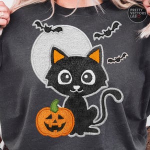 May include: Dark gray sweatshirt featuring a black cat with orange ears, a jack-o'-lantern, a full moon, and bats. The cat has large white eyes and a smiling face. The sweatshirt has the text "PRETTY VECTORS LAB" on the upper right.