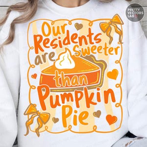 Op de afbeelding: Witte sweatshirt met de tekst "Our Residents are Sweeter than Pumpkin Pie" in oranje en bruin. Het ontwerp bevat een pompoentaartpunt, harten en strikken. Een grafisch T-shirt met herfstthema.