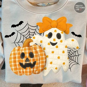 Op de afbeelding: Een lichtgrijs sweatshirt met een Halloween-thema. Het ontwerp bevat een lachende geest met een oranje strik, een geruite pompoen, spinnenwebben en vleermuizen. De geest is versierd met kleine oranje pompoenen.