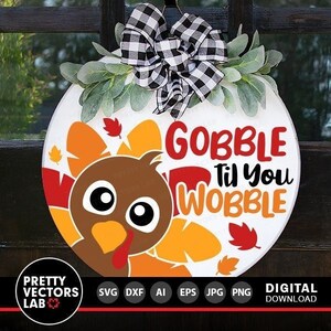 May include: A white round door hanger with a cartoon turkey with big eyes and a red wattle. The turkey is surrounded by orange and yellow feathers. The text "Gobble Til You Wobble" is written in red and black letters.