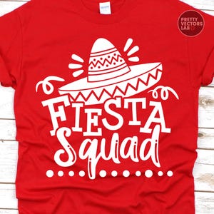 May include: A red t-shirt with a white graphic that says "Fiesta Squad." The design includes a sombrero and decorative elements. The shirt is made of a soft material and is suitable for casual wear.