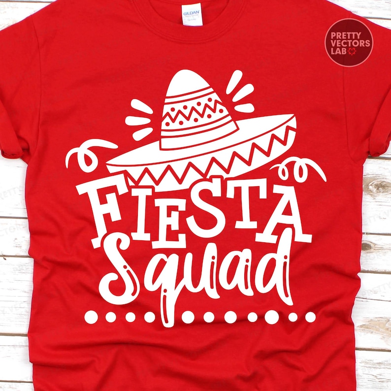 May include: A red t-shirt with a white graphic that says "Fiesta Squad." The design includes a sombrero and decorative elements. The shirt is made of a soft material and is suitable for casual wear.