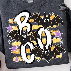 May include: A dark heather gray sweatshirt featuring a graphic print with the white text BOO, three black bats with white eyes, yellow horizontal stripes, and purple and white stars. The top right corner includes the text Pretty Vectors Lab.