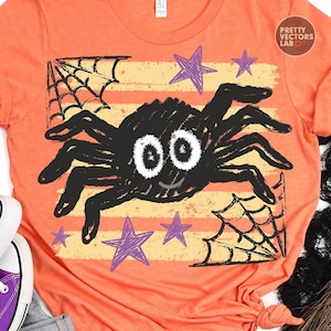 May include: An orange t-shirt featuring a graphic print of a black spider with large white eyes and a small smile. The design includes purple stars and black spiderwebs over horizontal yellow stripes. The text Pretty Vectors Lab is visible.