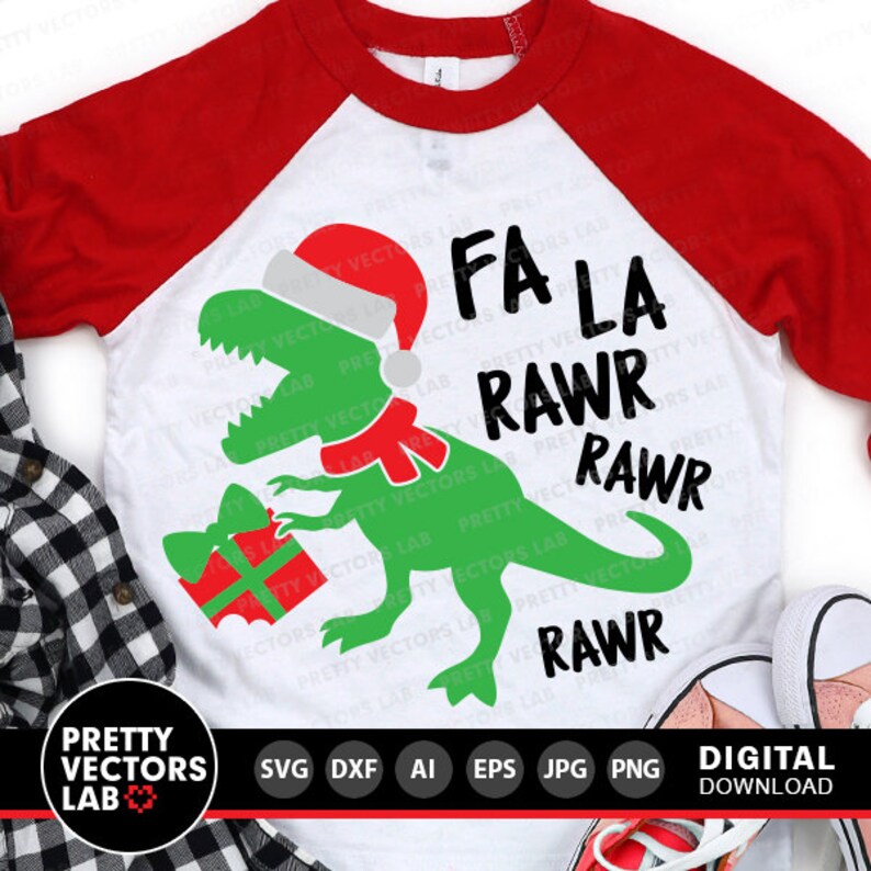 Puede incluir: Una camiseta de estilo b&eacute;isbol blanca y roja con un dinosaurio verde que lleva un gorro de Pap&aacute; Noel y sostiene una caja de regalo roja. El texto "Fa La Rawr Rawr Rawr" est&aacute; impreso en la camiseta.