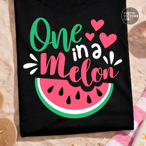 May include: A black t-shirt featuring the text One in a Melon in green and pink script and block lettering. The design includes three pink hearts and a graphic of a watermelon slice with a pink center, white rind, and green outer edge.