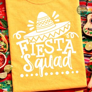May include: Yellow t-shirt with a white sombrero graphic and the words "FIESTA Squad". The design includes decorative elements and is likely for a festive occasion. The shirt is made of a soft material.