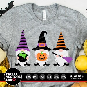 May include: Three gnomes dressed in Halloween costumes. The gnome on the left is holding a cauldron, the gnome in the middle is holding a jack-o-lantern, and the gnome on the right is holding a broom. The gnomes are wearing black and white striped hats, purple and black striped hats, and orange and black striped hats. The gnomes are on a grey t-shirt.
