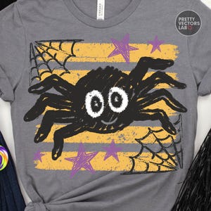 May include: A heather gray t-shirt featuring a graphic of a black spider with large white eyes, a small smile, and eight legs. The design includes yellow horizontal stripes, black spiderwebs in the corners, and purple hand-drawn style stars.