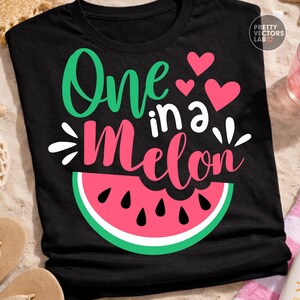 May include: A black short-sleeved t-shirt featuring the text One in a Melon in green and pink script and block lettering. The design includes three pink hearts and a graphic of a watermelon slice with black seeds at the bottom of the shirt.