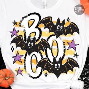May include: A white t-shirt featuring a graphic print with the word BOO in large black outlined letters. The design includes three black bats with white eyes and several purple stars over a background of horizontal yellow and white stripes.