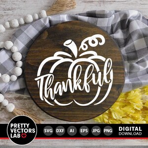 May include: A round wooden sign with a white pumpkin and the word "thankful" in a decorative script font.