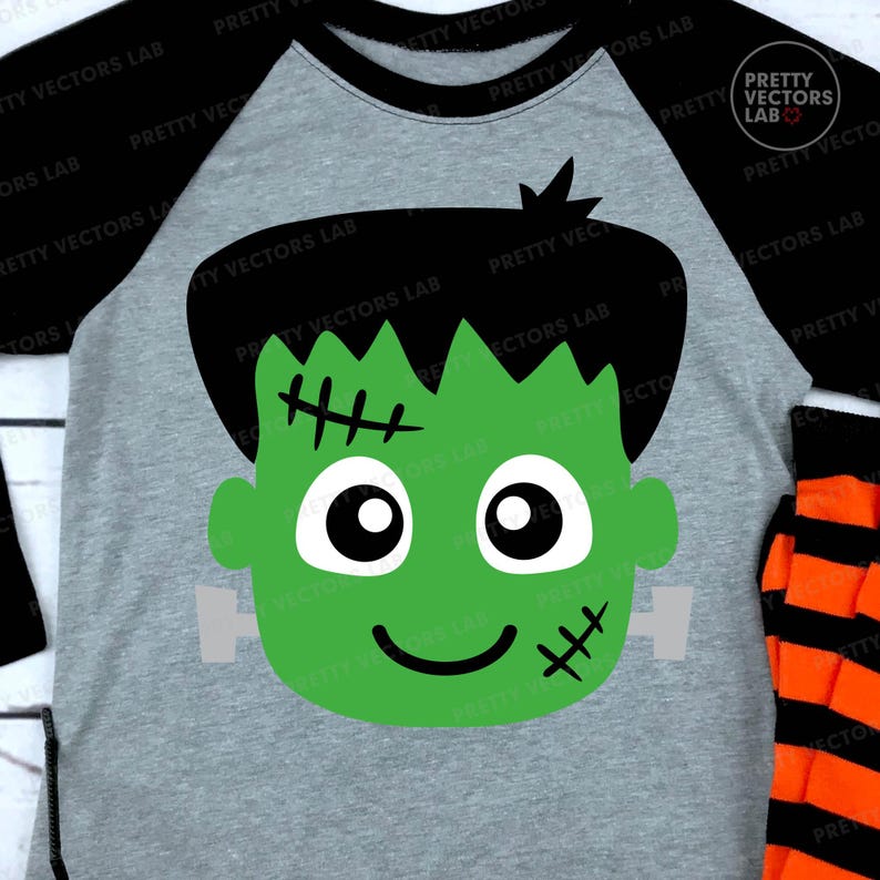 May include: A gray raglan-style shirt with black sleeves featuring a green Frankenstein's monster face graphic. The graphic includes black hair, stitches, and a smiling mouth. Orange and black striped pants are visible.