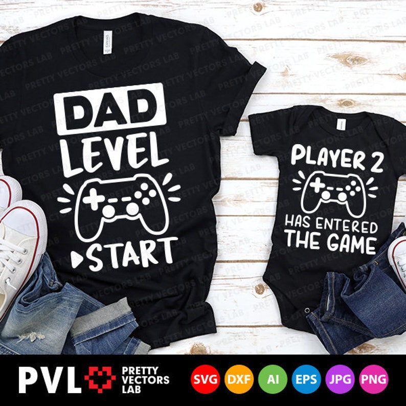 Op de afbeelding: Een zwart T-shirt met witte tekst die "Dad Level" zegt en een afbeelding van een videogamecontroller. Een zwarte romper met witte tekst die "Player 2 Has Entered The Game" zegt en een afbeelding van een videogamecontroller.