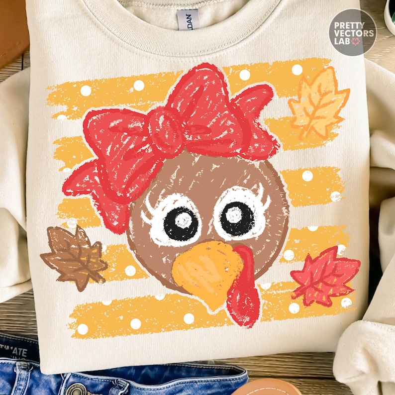 May include: A cream-colored crewneck sweatshirt featuring a graphic of a brown turkey face with a large red bow, white polka dots, and yellow stripes. The design includes three autumn leaves in shades of brown, yellow, and red, with a distressed texture.