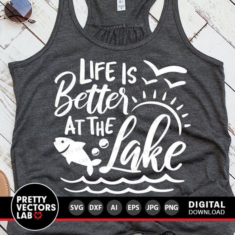 Puede incluir: Una camiseta sin mangas gris con el texto "Life is Better at the Lake" en blanco. El texto est&aacute; rodeado de un pez, un sol y olas.
