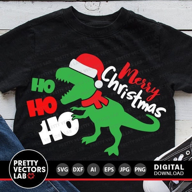 May include: A black t-shirt with a green dinosaur wearing a red Santa hat and a red scarf. The dinosaur is holding a sign that says "Ho Ho Ho" and the text "Merry Christmas" is above the dinosaur.