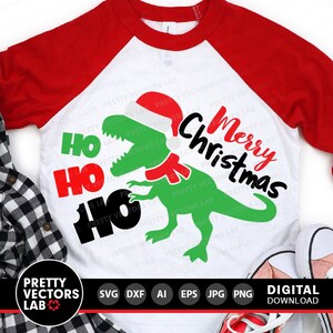 May include: A white and red Christmas themed t-shirt with a green dinosaur wearing a Santa hat and a red scarf. The text "Ho Ho Ho Merry Christmas" is printed on the shirt.