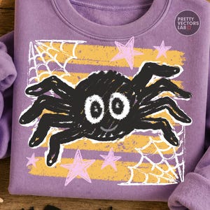 May include: A lavender sweatshirt featuring a central graphic of a black spider with large white eyes and a small smile. The design includes yellow horizontal stripes, white spiderwebs in the corners, and light pink stars. Text reads PRETTY VECTORS LAB.