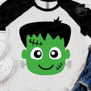 May include: A raglan-style t-shirt featuring a green Frankenstein's monster face graphic. The design includes black hair, stitches, and a smiling face. The shirt has a white body and black sleeves, perfect for Halloween.