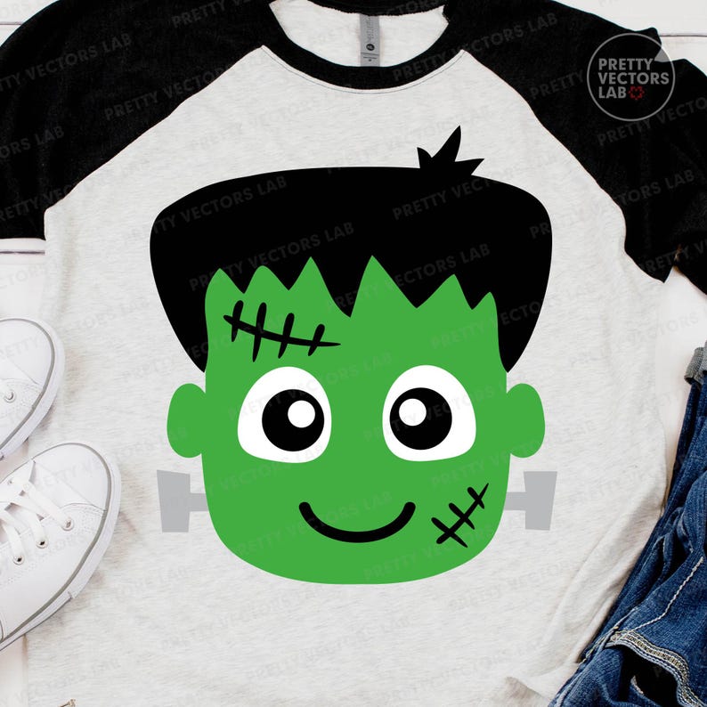 May include: A raglan-style t-shirt featuring a green Frankenstein's monster face graphic. The design includes black hair, stitches, and a smiling face. The shirt has a white body and black sleeves, perfect for Halloween.