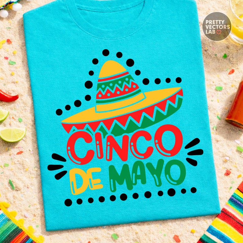 K&ouml;nnte beinhalten: Ein t&uuml;rkisfarbenes T-Shirt mit einem farbenfrohen Cinco de Mayo-Design. Die Grafik zeigt einen Sombrero, die Worte "Cinco de Mayo" in Rot, Gelb und Gr&uuml;n sowie schwarze Punkte.