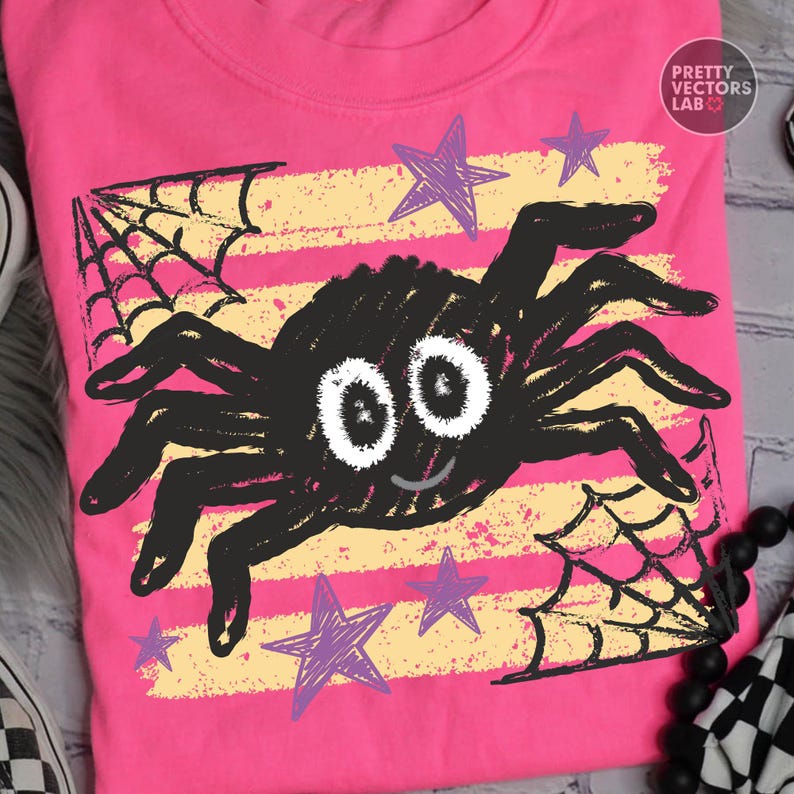 May include: A bright pink t-shirt featuring a central black spider graphic with large white eyes and a small smile. The design includes yellow horizontal distressed stripes, purple hand-drawn style stars, and black spiderwebs. Text reads PRETTY VECTORS LAB.