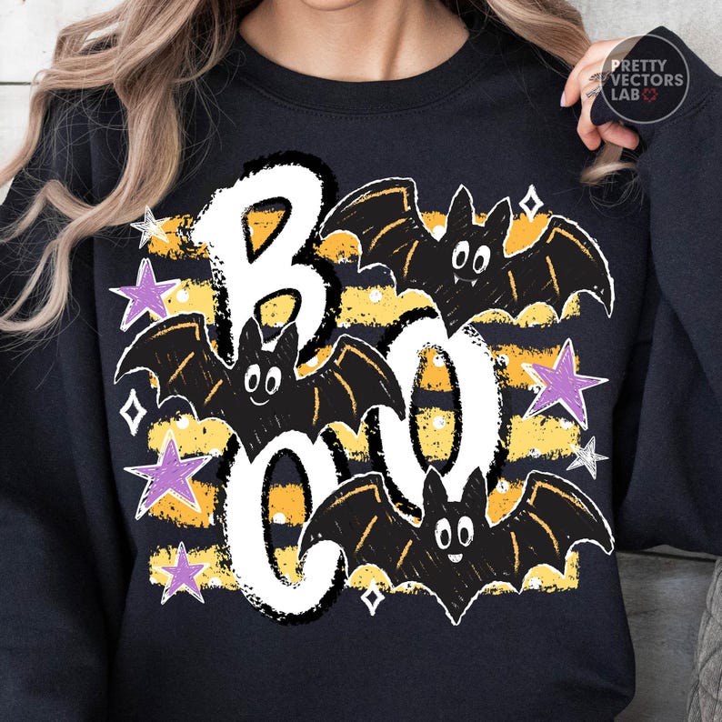 May include: A black long-sleeve sweatshirt featuring a graphic print with the word BOO in large white letters. The design includes three black bats, horizontal yellow and black stripes, and several purple and white stars surrounding the text.