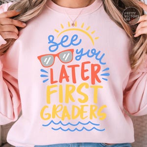 Puede incluir: Sudadera rosa claro con la frase "See you later First Graders" en azul, naranja y amarillo. El dise&ntilde;o incluye gafas de sol, un sol y olas, ideal para el regreso a clases o celebraciones de fin de curso.