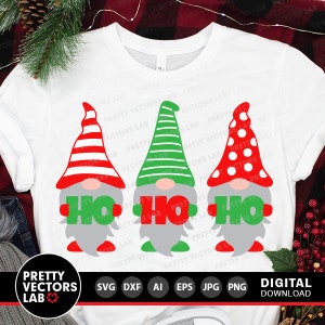 May include: Three gnomes wearing red, green, and white hats hold signs that say "Ho Ho" in red letters. The gnomes are on a white t-shirt.