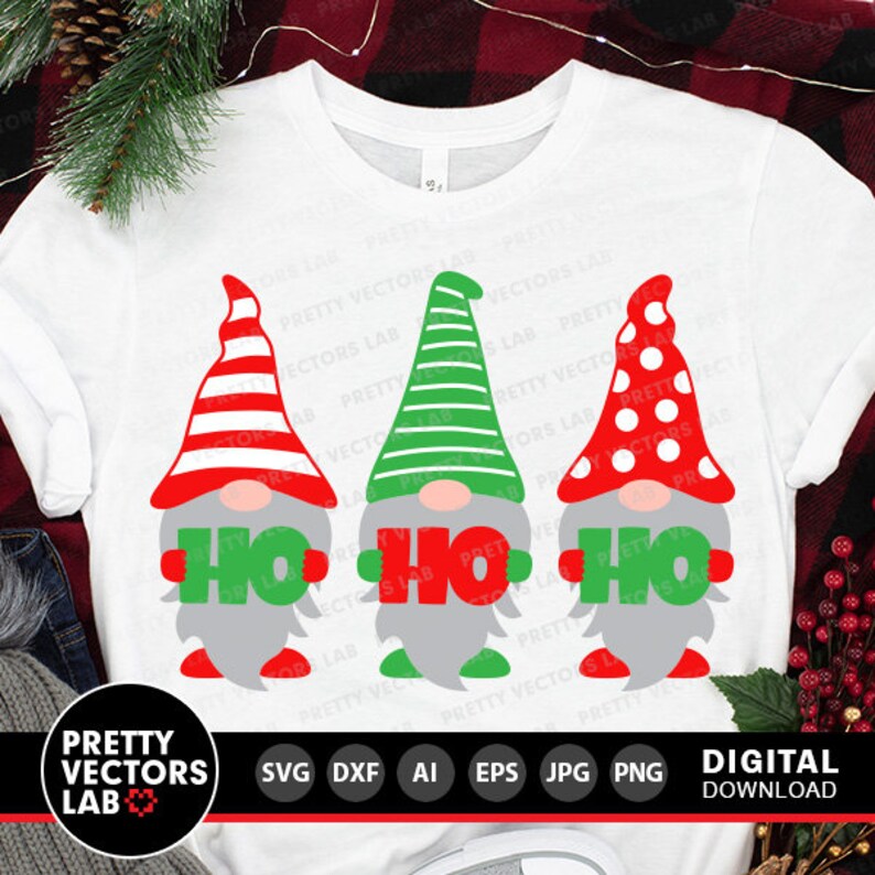 May include: Three gnomes wearing red, green, and white hats hold signs that say "Ho Ho" in red letters. The gnomes are on a white t-shirt.
