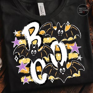 May include: A black t-shirt featuring a graphic design with the word BOO in large white letters. The design includes three black bats with white eyes, yellow horizontal stripes, and several purple and white stars scattered around the text.
