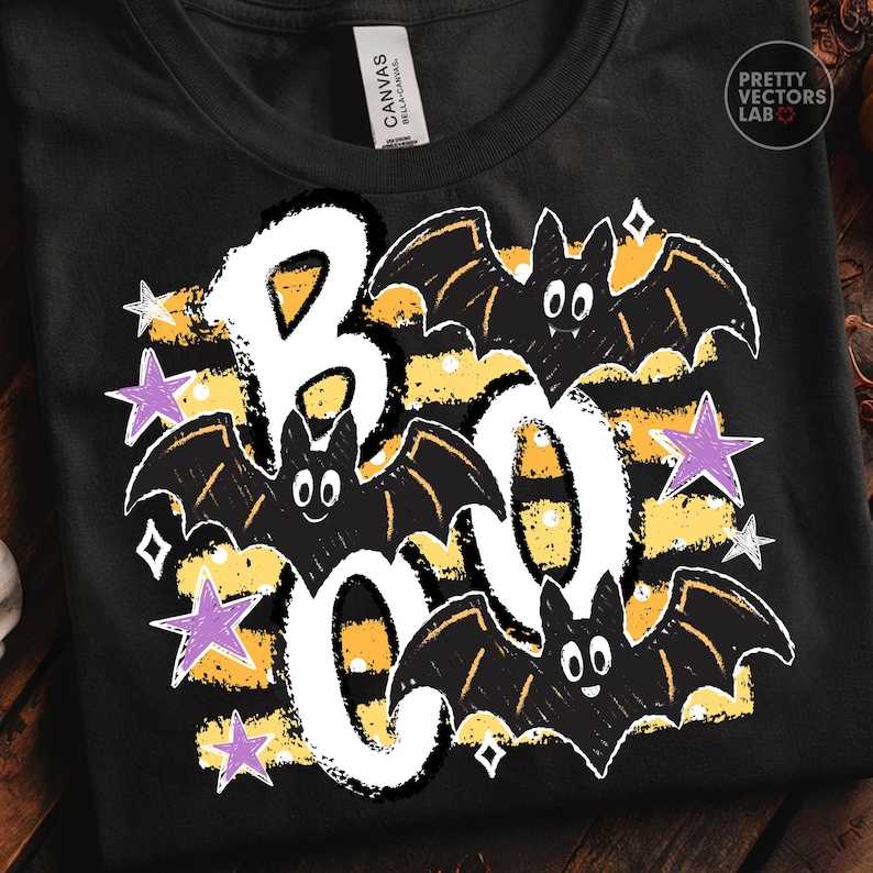 May include: A black t-shirt featuring a graphic design with the word BOO in large white letters. The design includes three black bats with white eyes, yellow horizontal stripes, and several purple and white stars scattered around the text.