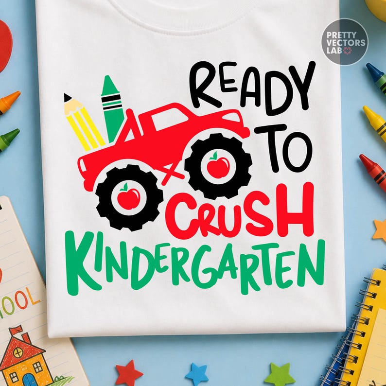Puede incluir: Una camiseta blanca con un gr&aacute;fico de un cami&oacute;n monstruo rojo con neum&aacute;ticos negros, cada uno con un icono de manzana roja. El dise&ntilde;o incluye un l&aacute;piz amarillo, un cray&oacute;n verde y el texto READY TO CRUSH KINDERGARTEN en letras negras y rojas.