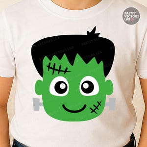 May include: White t-shirt featuring a green Frankenstein's monster face graphic. The design includes black hair, stitched details, and a smiling expression. The text "PRETTY VECTORS LAB" is visible.